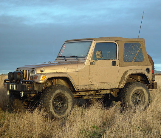 Mud-covered Jeep Wrangler YJ parked in a field.